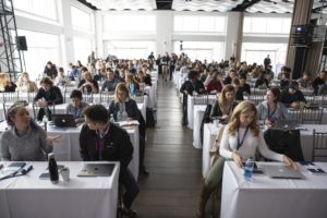 audience seating at classroom tables in white linens and people chatting with each other