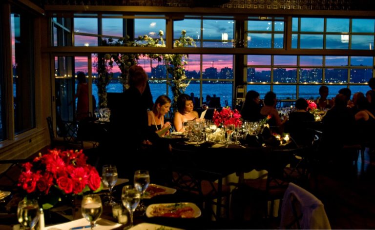 Pre set first course on the tables, guests starting to sit down, sunset in the background and hudson river