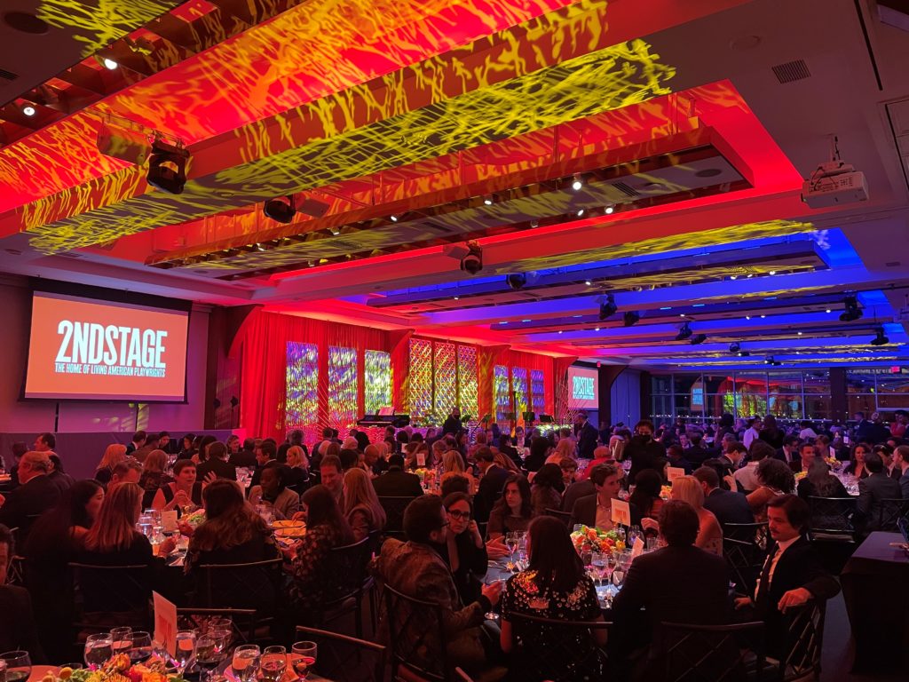 Gala guests at dinner rounds under a neon ceiling installation at Pier Sixty, Chelsea Piers