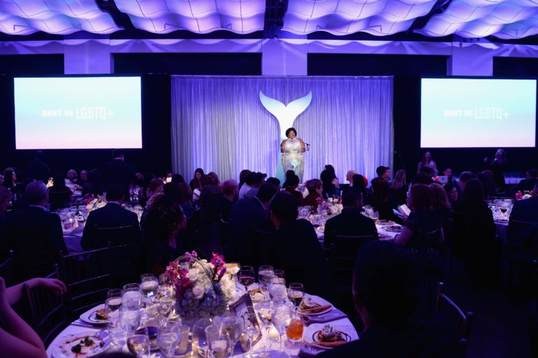 guests eating dinner at round tables while speaker is on stage and she is presenting.