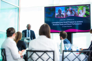 Speaker up front next to a screen with a presentation talking/presenting to the audience at Pier Sixty