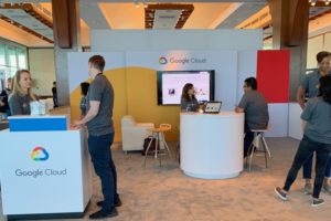 Exhibit booth in white with people working the booth and attendees walking by