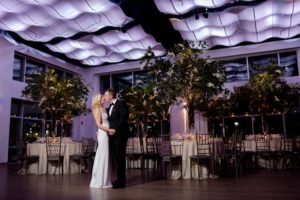 Bride and groom kissing in the ballroom by dinner tables