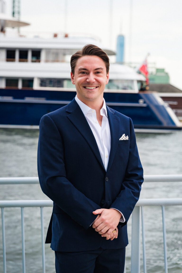 John Young smiling by the waterfront with the Manhattan skyline in the background at The Pier Sixty Collection